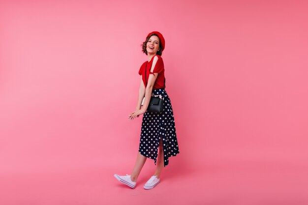 Full-length portrait of glad european woman in white sport shoes. laughing blithesome girl in french red beret.