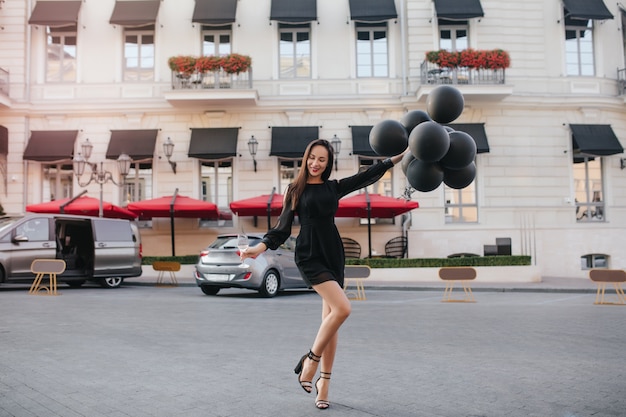 Free Photo full-length portrait of gorgeous dark-haired woman in elegant shoes dancing with party balloons on the street