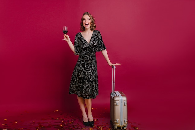 Портрет изящной белой женщины в полный рост, пьющей вино перед поездкой