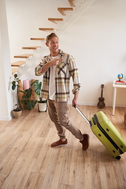 Free photo full length portrait of handsome smiling man pointing finger at someone leaving the apartment with