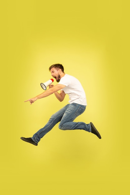 노란색 배경에 고립 행복 점프 남자의 전체 길이 초상화. 캐주얼 옷에 백인 남성 모델입니다. 선택의 자유, 영감, 인간의 감정 개념. 마우스 피스로 부르기.