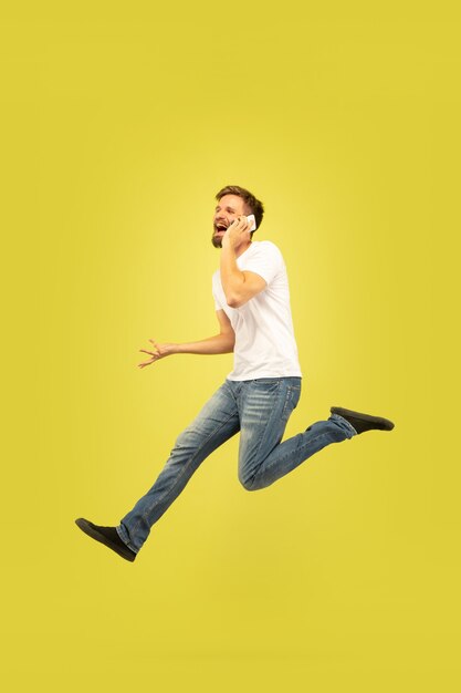 노란색 배경에 고립 행복 점프 남자의 전체 길이 초상화. 캐주얼 옷에 백인 남성 모델입니다. 선택의 자유, 영감, 인간의 감정 개념. 서둘러, 전화 통화.
