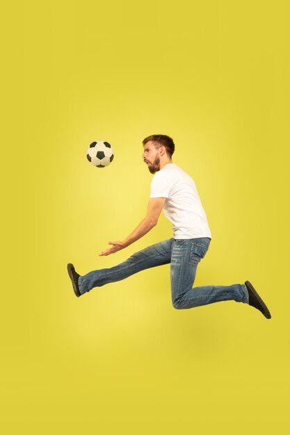 Full length portrait of happy jumping man isolated on yellow background. Caucasian male model in casual clothes. Freedom of choices, inspiration, human emotions concept. Playing football on the run.