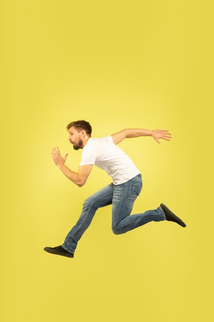 Полнометражный портрет счастливого прыгающего человека, изолированного на желтом фоне. Кавказская мужская модель в повседневной одежде. Свобода выбора, вдохновение, концепция человеческих эмоций. Беги за продажами, поторопись.