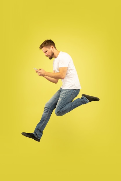 Full length portrait of happy jumping man isolated on yellow background. Caucasian male model in casual clothes. Freedom of choices, inspiration, human emotions concept. Winning in sport bet.
