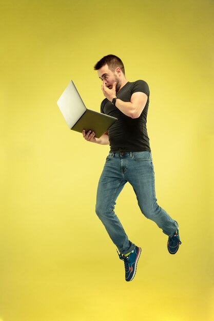Full length portrait of happy jumping man with gadgets isolated on yellow background