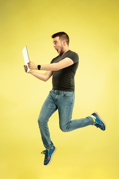 Full length portrait of happy jumping man with gadgets isolated on yellow.