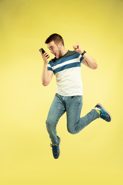 Full length portrait of happy jumping man with gadgets on yellow background