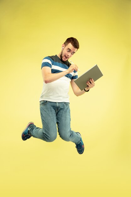 Full length portrait of happy jumping man with gadgets on yellow.