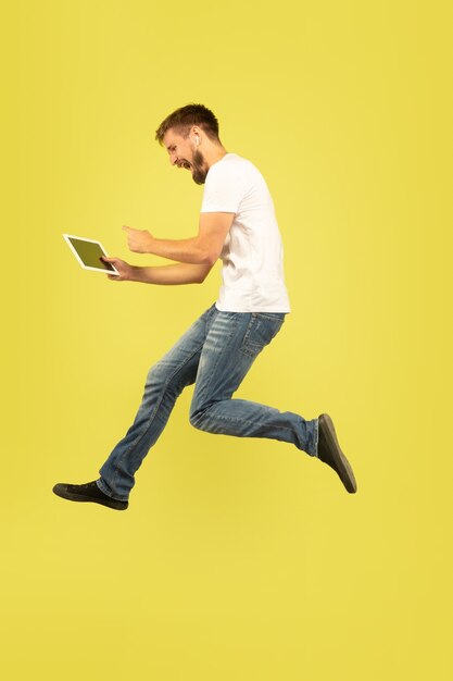 Full length portrait of happy jumping man on yellow background