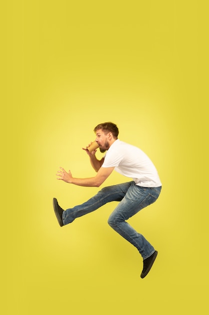 Full length portrait of happy jumping man on yellow wall