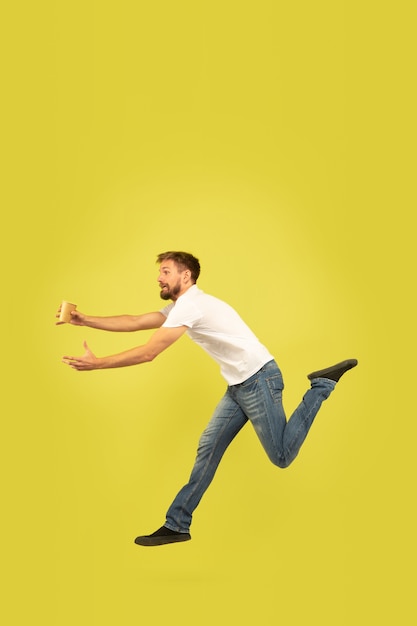 Full length portrait of happy jumping man on yellow wall