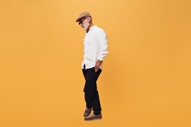 Full length portrait of man in white shirt and black pants on orange background Photo of bearded grayhaired adult guy in fashionable clothes