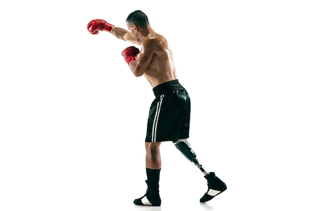 Full length portrait of muscular sportsman with prosthetic leg, copy space. Male boxer in red gloves. Isolated shot on white wall.