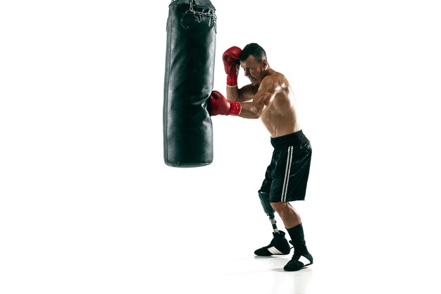 Full length portrait of muscular sportsman with prosthetic leg, copy space. Male boxer in red gloves training and practicing. Isolated on white  wall. Concept of sport, healthy lifestyle.