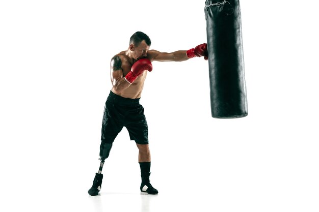 Full length portrait of muscular sportsman with prosthetic leg, copy space. Male boxer in red gloves training and practicing. Isolated on white  wall. Concept of sport, healthy lifestyle.