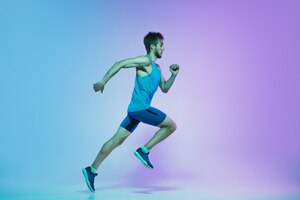 full length portrait of active young caucasian running, jogging man on gradient studio in neon light