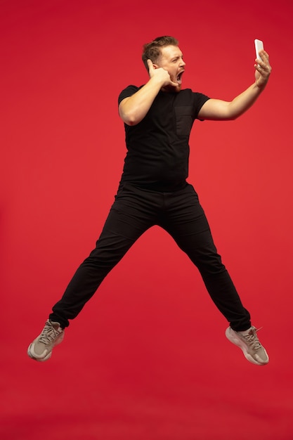 Бесплатное фото Полнометражный портрет молодого человека прыжков в высоту изолированного на красной стене. модель кавказского мужчины. copyspace. человеческие эмоции, выражение лица, спортивная концепция.