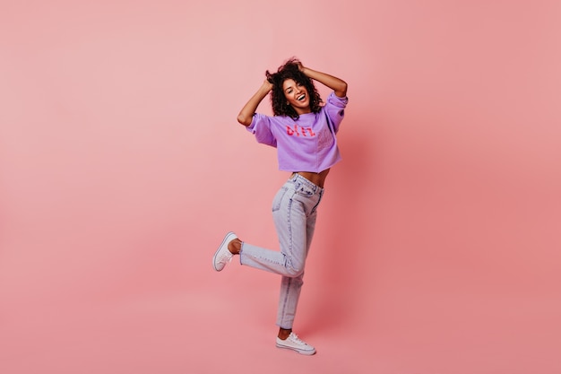 Full-length portrait of optimistic laughing woman dancing in studio. Relaxed curly female model enjoying life.