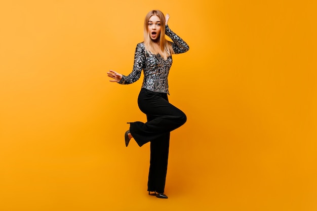 Full-length portrait of pleasant woman in stylish black pants. portrait of surprised glamorous woman isolated on orange