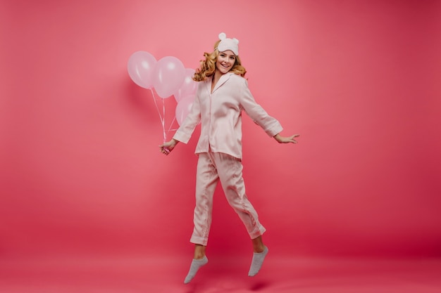 Full-length portrait of pleased fair-haired lady relaxing after party. indoor photo of positive birthday girl expressing energy on pink wall.