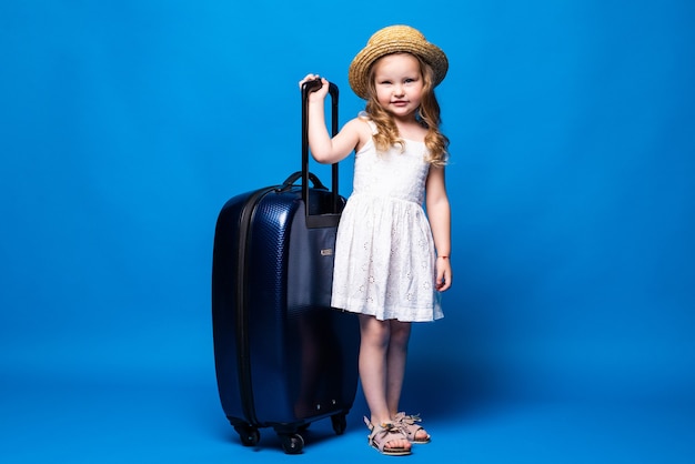 파란색 벽에 고립 된 수하물 예쁜 꼬마 소녀의 전체 길이 초상화. 주말 휴가에 해외로 여행하는 승객. 항공 비행 여행 개념.