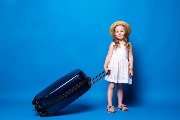 파란색 벽에 고립 된 수하물 예쁜 꼬마 소녀의 전체 길이 초상화. 주말 휴가에 해외로 여행하는 승객. 항공 비행 여행 개념.