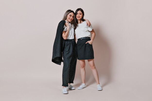 Full-length portrait of sisters in similar outfits in polka dots posing against isolated wall