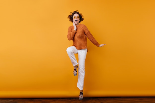 Full-length portrait of slim curly woman in casual outfit posing on one leg