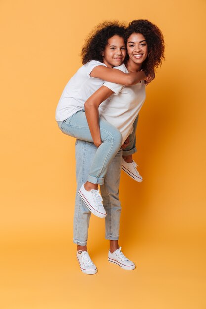 Full length portrait of smiling african girl carrying sister