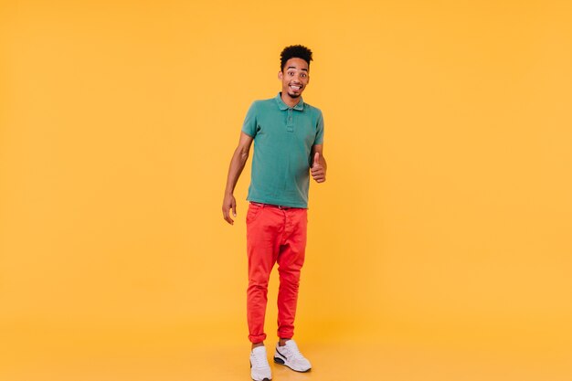 Full-length portrait of stylish african guy in white sneakers. Glad brunette man standing in confident pose.