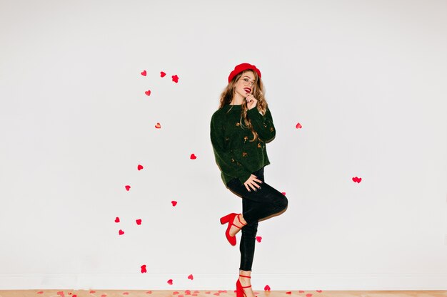 Full-length portrait of stylish woman posing on one leg in light room decorated with hearts