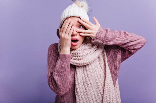 Full-length portrait of well-dressed girl in black pantyhose plays with lush skirt. Indoor photo of cute woman in long scarf and sweater posing on purple wall.