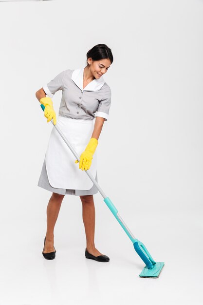 Full length portrait of young attractive woman in uniform cleaning floor with mop