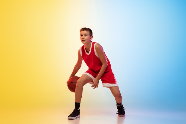 Full length portrait of a young basketball player with ball on gradient background