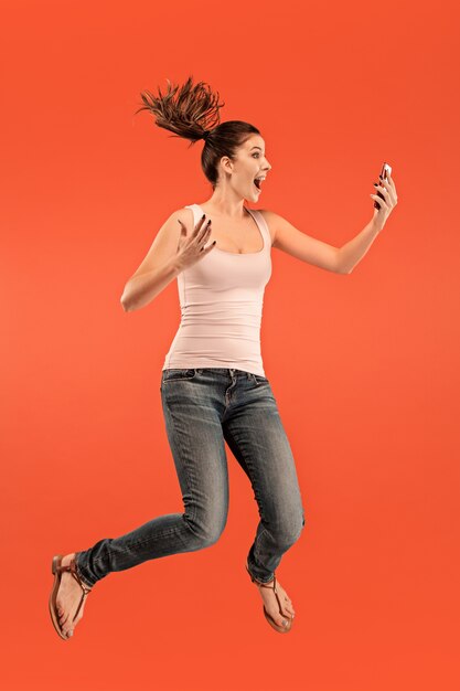 Полная длина довольно молодой женщины принимая телефон, прыгая на красном фоне студии.
