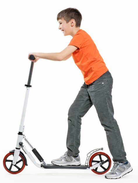 Full length profile of a happy kid riding a scooter isolated on white background