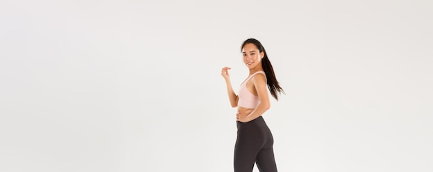 Full length profile portrait of sassy slim brunette asian girl doing fitness workout in gym walking