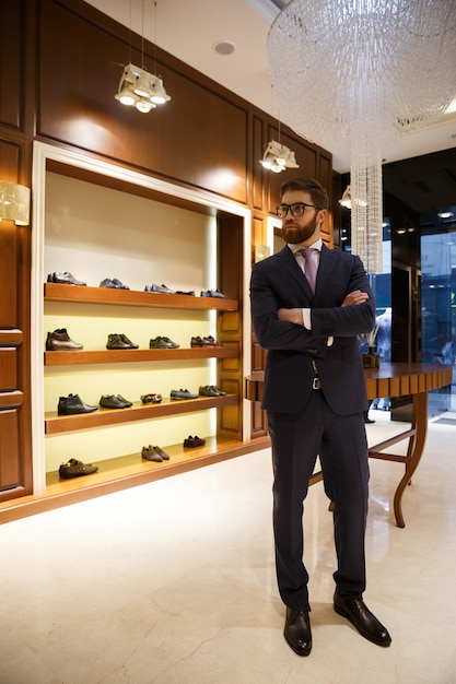 Free photo full-length shot of bearded man in suit and glasses standing in wardrobe and looking away