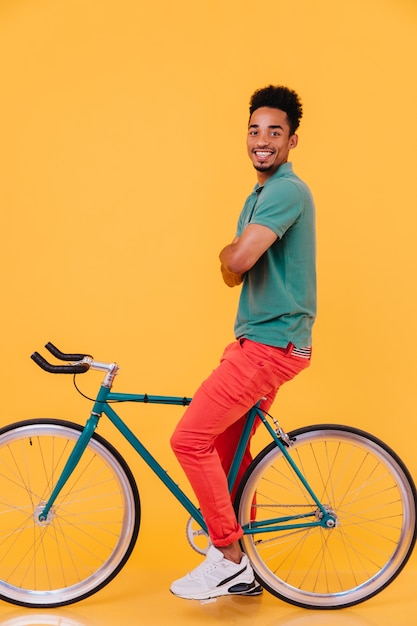 Full-length shot of confident black guy sitting on his bicycle with arms crossed. Portrait of pleased african man relaxing.