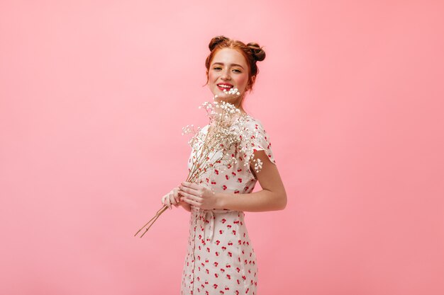 Full-length shot of cute lady in midi dress and heeled sandals. Woman holding white flowers on pink background.