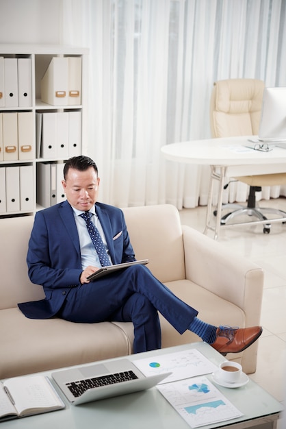 Full length shot of entrepreneur sitting on sofa with digital tablet