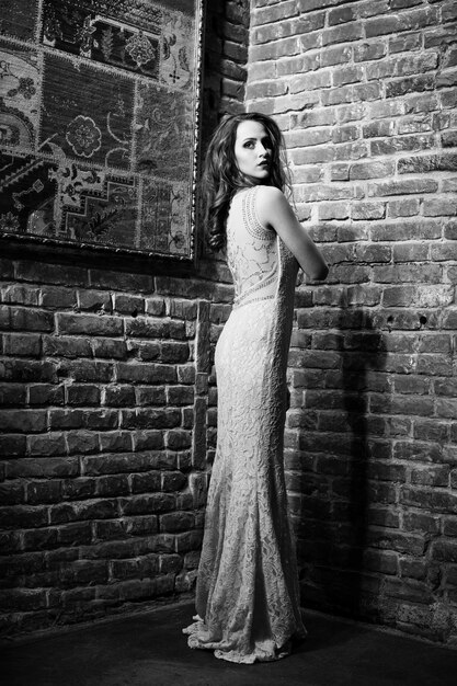 Полнометражный снимок модной девушки-модели на персиковом вечернем платье на фоне кирпичной стены