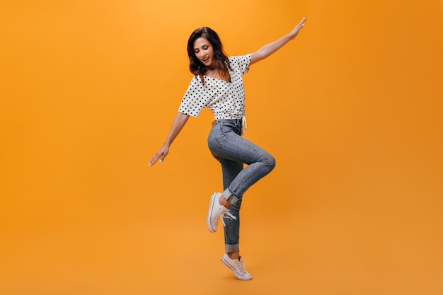 Full-length shot of girl in jeans and T-shirt on orange background