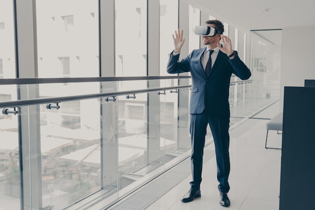 사무실에 서서 vr 기술을 사용하고 3d 고글을 착용하고 동료와 가상 회의에 참여하는 우아한 정장을 입은 성공적인 미남 비즈니스 전문가의 전체 길이 샷