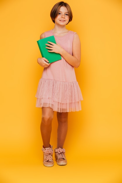 Full-length shot of smiling girl holding green book isolated