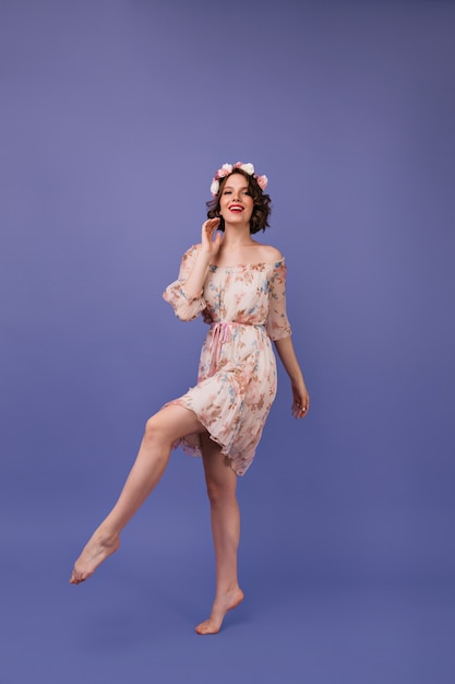 Full-length shot of wonderful girl in summer dress. Well-dressed young woman in circlet of flowers dancing.