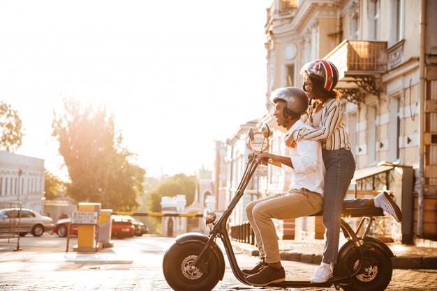 Full length side view of happy african couple rides on modern motorbike on the street