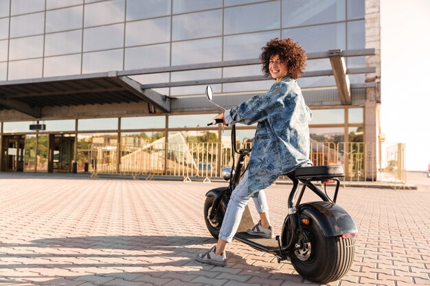 Full length side view of pleased curly woman sitting on motorbik-