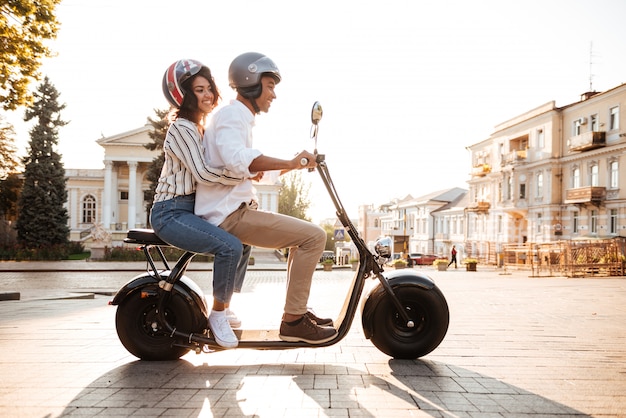 路上で現代のバイクに乗る若いアフリカカップルの完全な長さの側面図